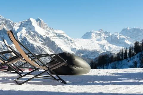 Empty deckchairs stand in the snow against the backdrop of snow-capped mountains Stock Photos