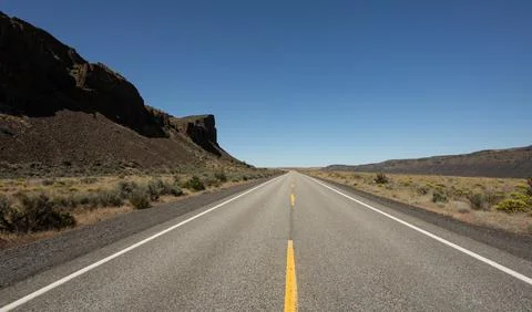 Empty Desert Highway Through Rocky Canyon Landscape Under Clear Blue Sky Stock Photos