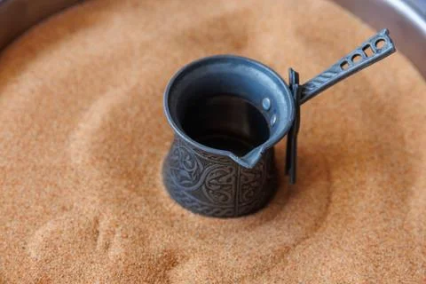 Empty designed metal coffee pot set within bed of sand, capturing the traditi Stock Photos