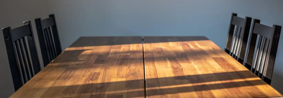 Empty dining table and dark chairs. Natural light across wooden surface. Stock Photos