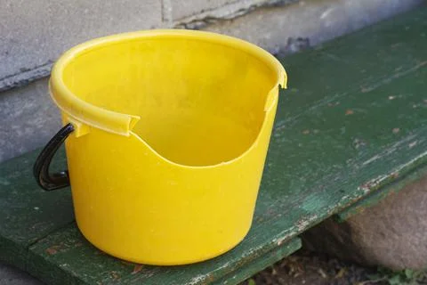Empty dirty broken yellow plastic bucket on green bench. 스톡 사진