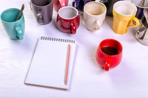 Empty dirty coffee cups, different colors on the table and a notebook for wri Stock Photos