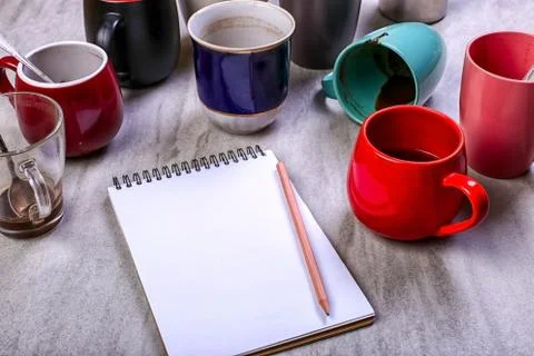 Empty dirty coffee cups, different colors on the table and a notebook for wri Stock Photos