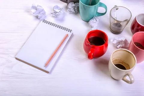 Empty dirty coffee cups, different colors on the table and a notebook for wri Stock Photos