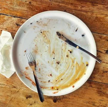 Empty dirty plate with fork and knife on the wooden table and crumpled napkin Stock Photos