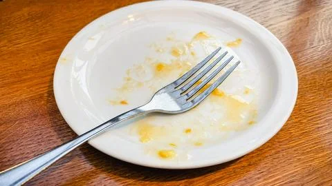Empty dirty white plate with a fork and food leftovers on a wooden table af.. Stock Photos