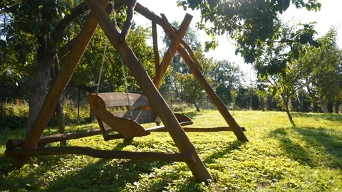 An empty, double swing is swinging in the sunny garden. Stock Footage 113499984
