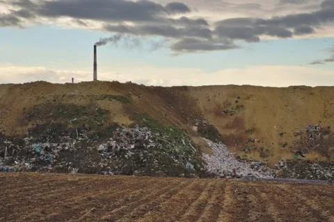 Empty farm field with garbage, waste dump and chimney at background Stock Photos