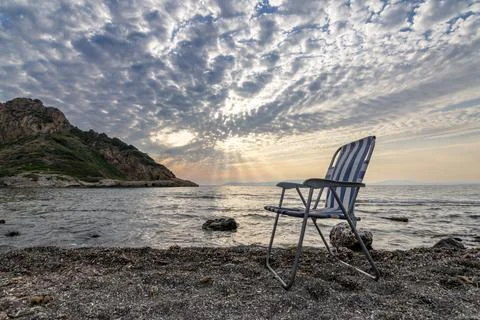 Empty Folding Beach Chair on Pebble Shore at Sunset Stock Photos