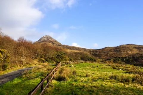 Empty footpath between meadows leading to mountains in far distance, blue sky Stock Photos