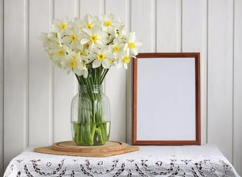 Empty frame and white daffodils in a glass jug. Stock Photos