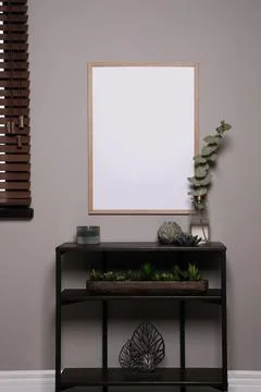 Empty frame hanging on grey wall over wooden console table with decor. Mockup Stock Photos