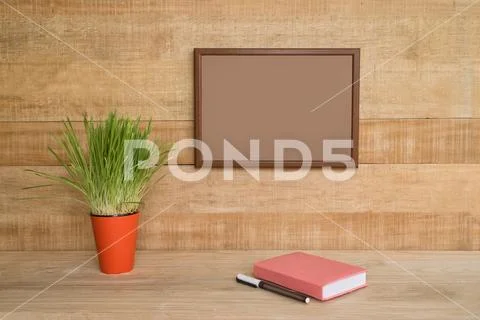 Empty frame on a wooden wall. Notebook and pen, green houseplant on the table Stock Photos