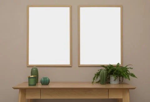 Empty frames hanging on beige wall over wooden table with decor. Mockup for d Stock Photos