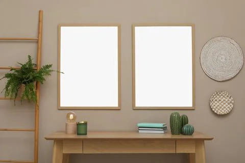 Empty frames hanging on beige wall over wooden table with decor. Mockup for d Foto stock