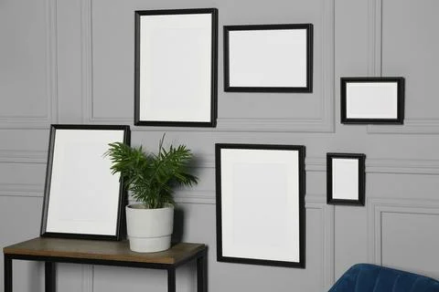 Empty frames hanging on grey wall near wooden table indoors Stock Photos