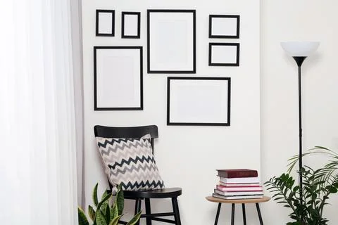 Empty frames hanging on white wall, wooden chair and table with books indoors Foto stock