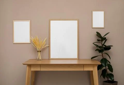 Empty frames, wooden table and plant near pale rose wall. Mockup for design 스톡 사진