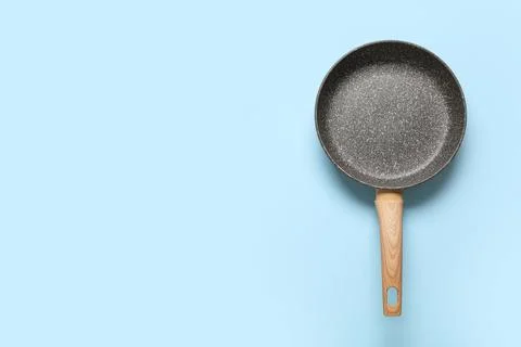 Empty frying pan with non-stick coating and wooden handle on light blue backg Photos