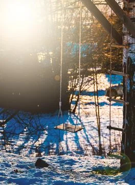 Empty garden swing in the sunset light with snowy ground. 스톡 사진