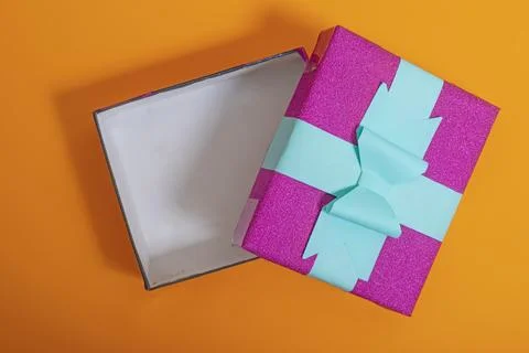 Empty gift box with colorful wrapping and bow against a bold orange backdro.. Stock Photos