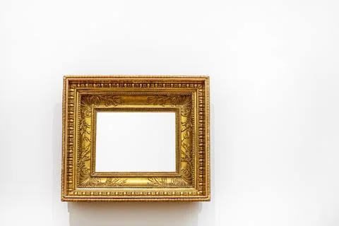 An empty gilded frame. An antique frame with a wide profile on a light wall.. Stock Photos