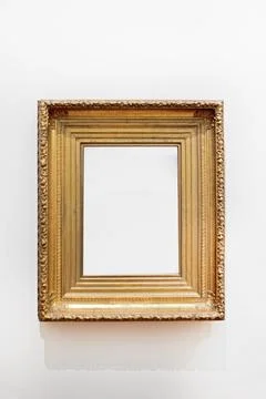 Empty gilded frame on a light wall. Mockup for signage and advertising. Stock Photos