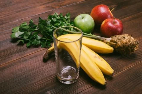 Empty glass, bananas, celery root and apples on a dark wooden table Stock Photos