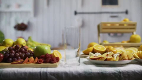 Empty glass between plates of oranges and other fruit at kitchen counter, Stock Footage 341189972