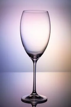 Empty glass goblet without wine on a thin leg stands on a mirror surface. Stock Photos