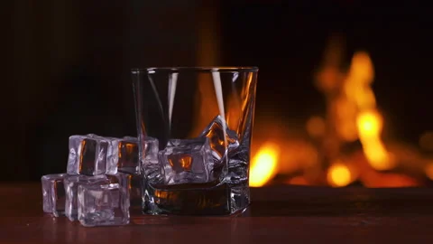 Empty glass with ice stands on a table. Background of a fireplace with flame Stock-Footage 148076010
