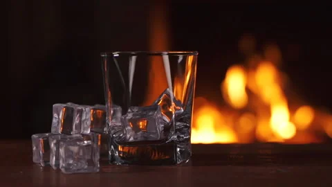 Empty glass with ice stands on a table. Background of a fireplace with flame Stock-Footage 157123627