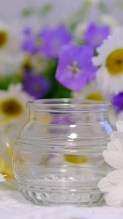 Empty glass jar surrounded by white daisies and blue wildflowers creating Stock Footage 344894758