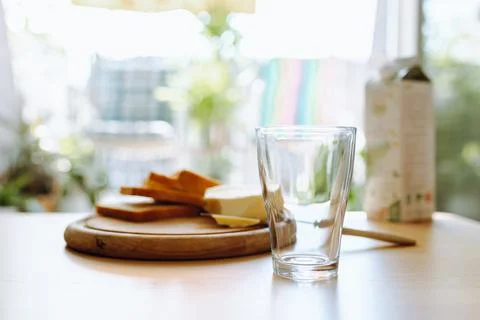 An empty glass stands on table, in background there is bread, butter, milk... Fotos de archivo