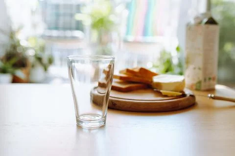 An empty glass stands on table, in background there is bread, butter, milk... Photos