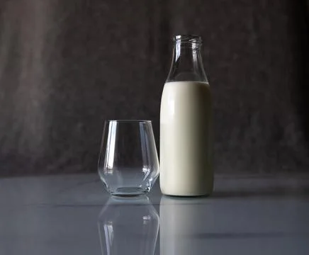 An empty glass is on the table next to a full bottle of milk. Stock Photos