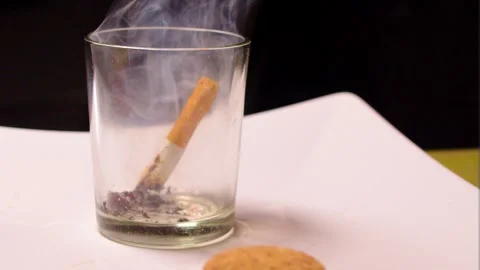 Empty glass with tiny bit of ash placed on white paper with black Video stock 252632340