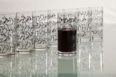 Empty glasses with pattern in row with one filled with drink Foto stock