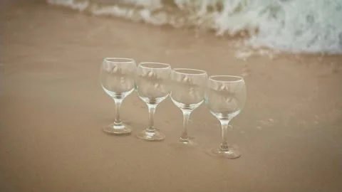 Empty glasses for wine falls in water because of ocean waves washed they on sand Stock Footage 252290214