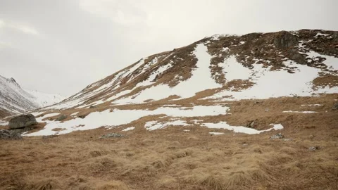 Empty golden valley meadow with scattered snow patches leading up toward a Stock Footage 344183278