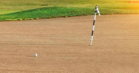 Empty golf field with a ball close to the hole, in it there is a checkered flag. Stock Photos