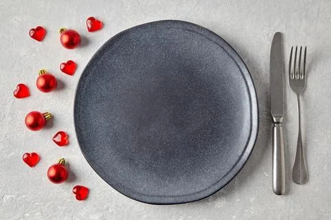 An empty gray ceramic plate with cutlery surrounded by red christmas balls and Stock Photos