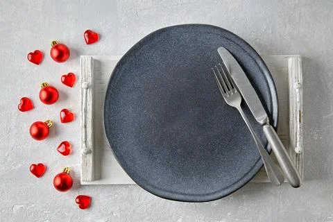 An empty gray ceramic plate on a white tray with cutlery surrounded by red Stock Photos