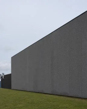 An empty gray wall on a warehouse building in gray concrete and a lawn in the Stock Photos