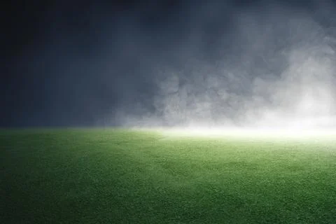 An empty green grass turf field illuminated by a bright spotlight under a d.. Stock Photos