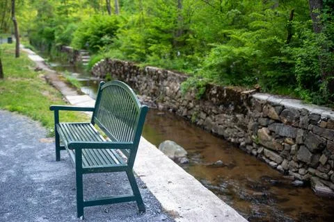 Empty green park bench alongside a canal with water and stone walls Stock Photos