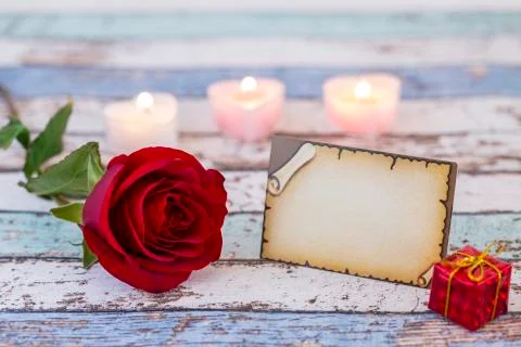Empty greeting card with single red rose, gift box, and candles Stock Photos