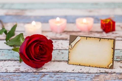 Empty greeting card with single red rose, gift box, and candles Stock Photos