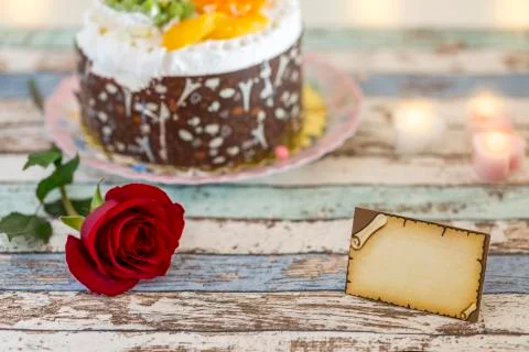 Empty greeting card, single red rose, and birthday cake on turquoise table Stock Photos