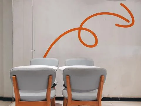 Empty grey chairs and tables set against a white wall with orange abstract graph Stock Photos